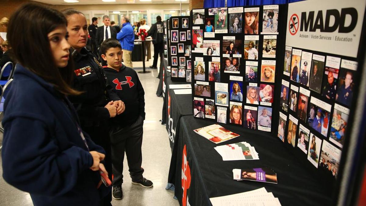 Arlington Police Officer Stacie Brown, with her niece Ashleigh Konig and her nephew Ryan Konig, look at display board that feature photos of victims and survivors of drunk driving accidents at the M.A.D.D 2015 Candlelight Vigil and National Day of Remembrance at the University of Texas at Arlington Maverick Activities Center Thursday, Dec. 3, 2015.
