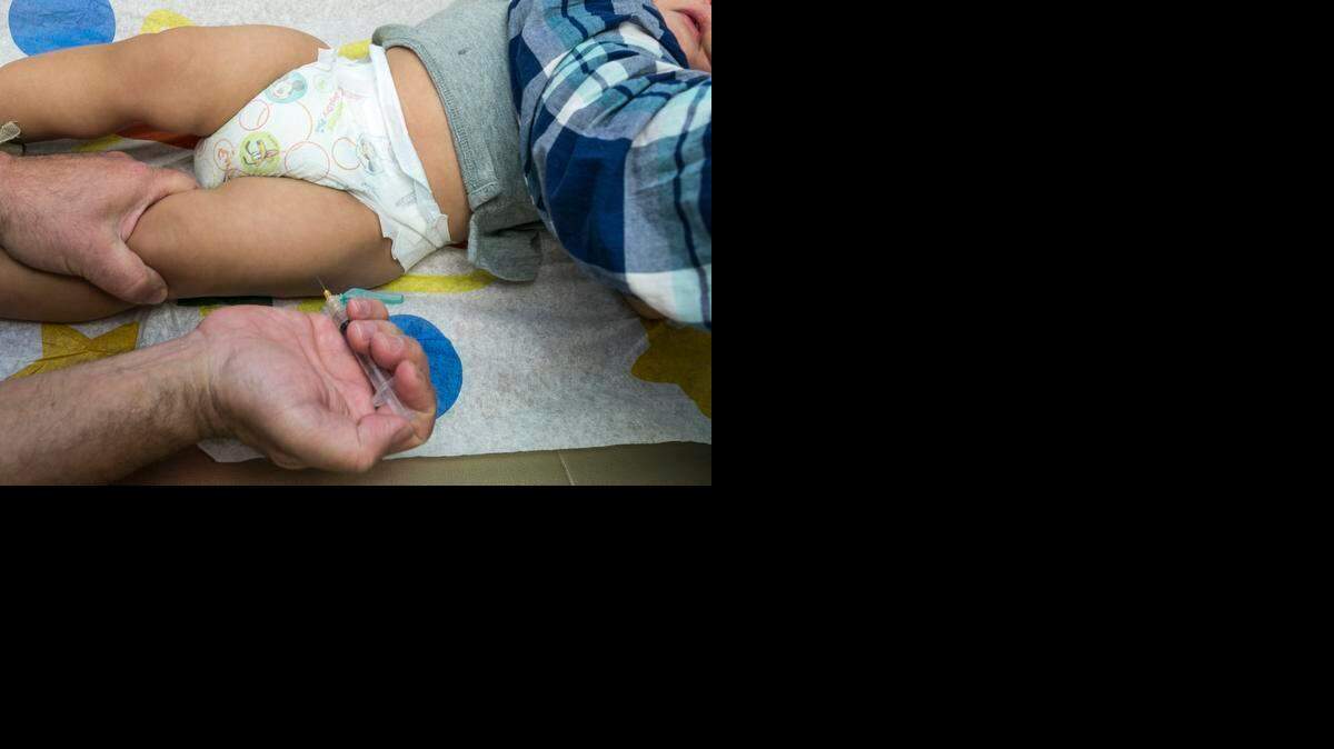 
A pediatrician uses a syringe to vaccinate a 1-year-old with the measles-mumps-rubella (MMR) vaccine. 
