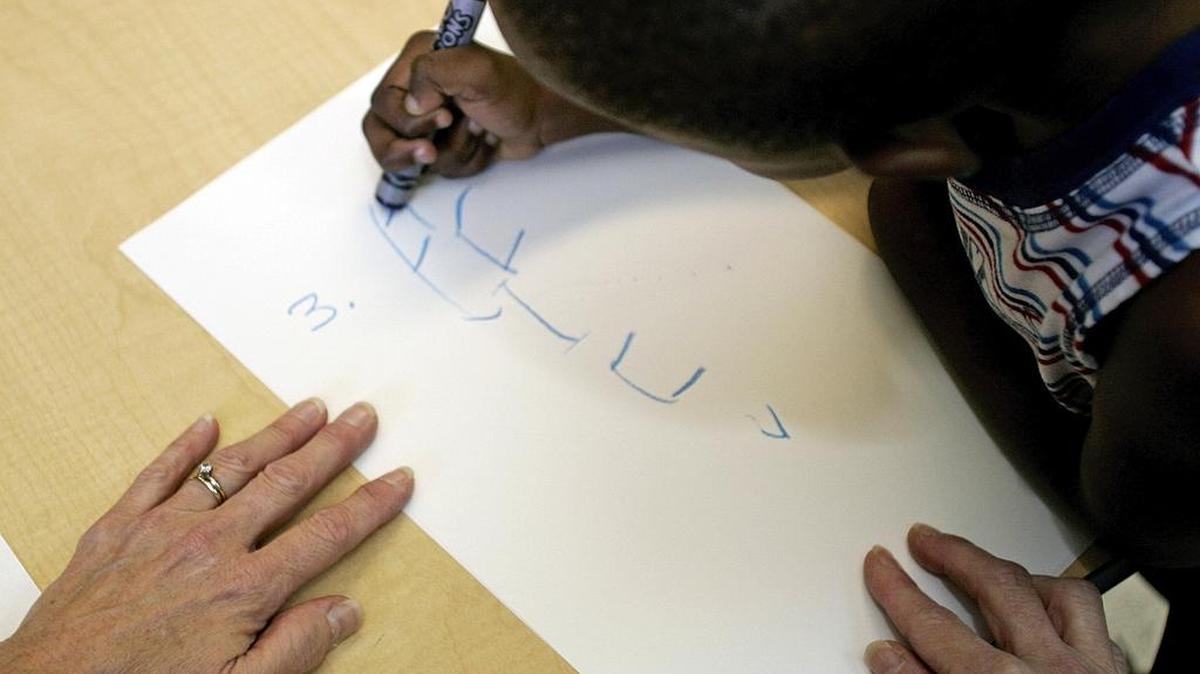 A student prints his name with a big crayon in a pre-K class at The Children’s Place in Arlington.