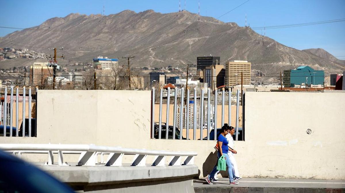 Pedestrians walk along a street in Ciudad Juarez, with El Paso in the background.