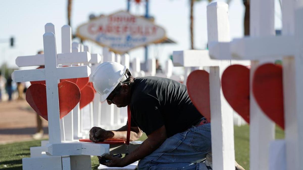 Greg Zanis writes the name of a victim of Sunday's shooting as he places crosses near the Las Vegas sign .