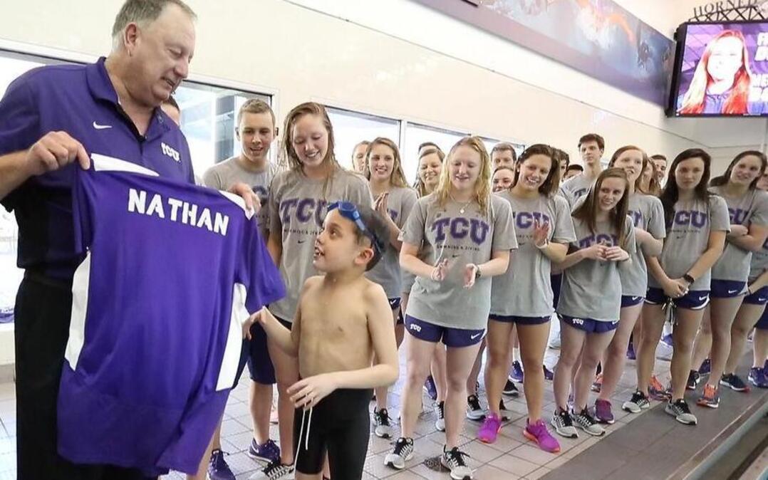 Nathan Lin, 8, gets a personalized TCU shirt from swim coach Richard Sybesma as Frogs team members watch.