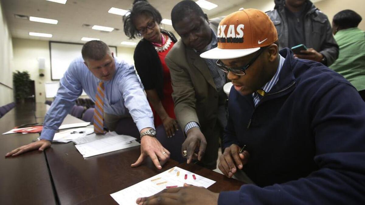 Former Arlington Bowie standout Tope Imade gets help from his coach, Nate Van Cleave, left, and mom and dad, Betty and Felix Imade during National Signing Day at the Arlington ISD Professional Development Center in Arlington, Texas on Wednesday, Feb. 3, 2016.