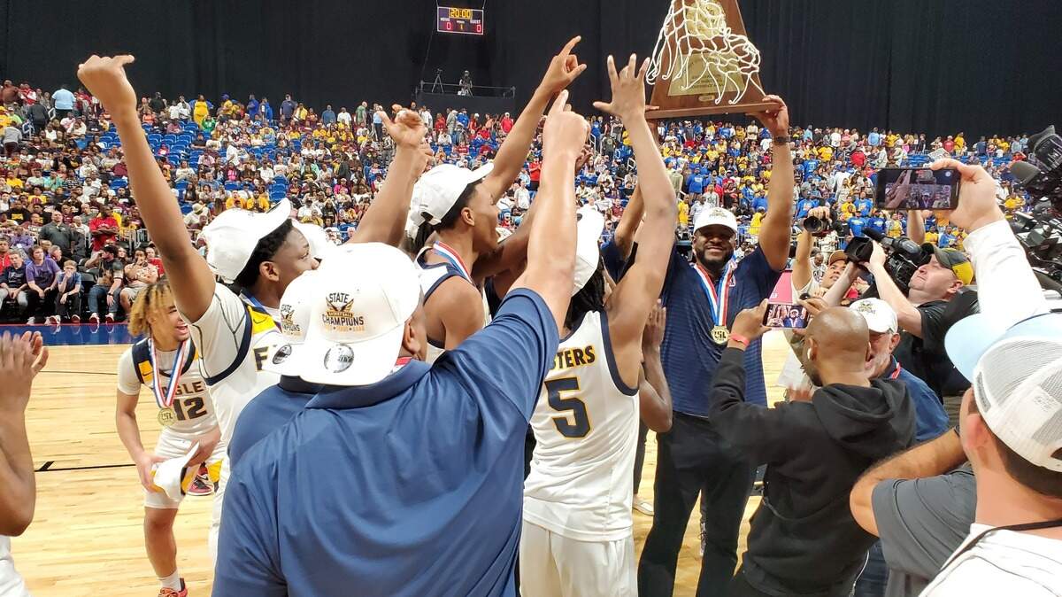 Dallas Oak Cliff Faith Family coach Brandon Thomas holds up the Class 4A state championship trophy in front of his players after defeating Houston Washington on Saturday, March 11, 2023 at the Alamodome in San Antonio, Texas.