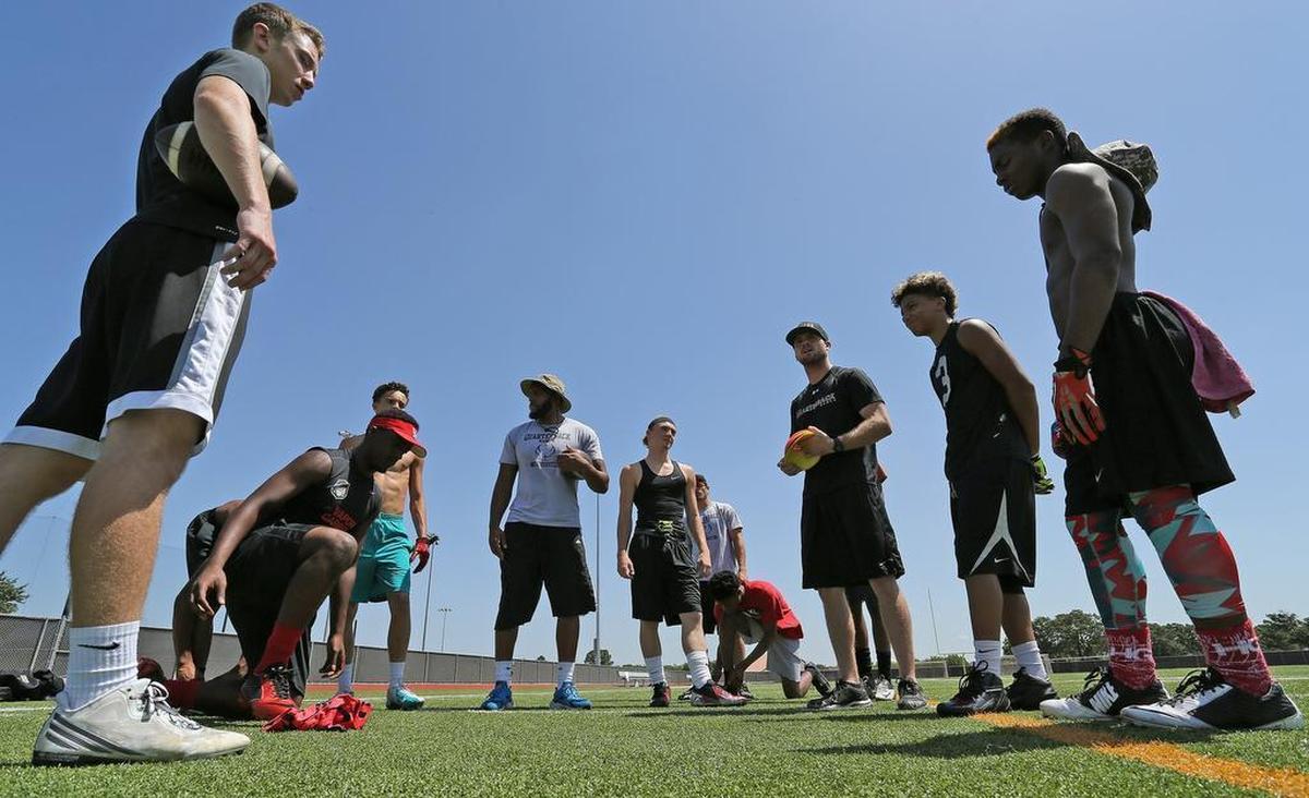 Instructor Nate Poppell, third from right, works with quarterbacks and receivers during a session at Euless Trinity High School. 