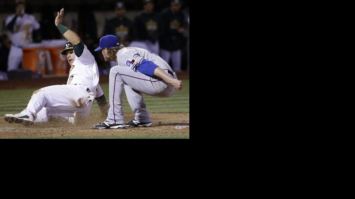 
Josh Phegley slides in safely for an Oakland run in a fourth inning in which the Rangers committed three errors and a passed ball behind Ross Detwiler, right.
