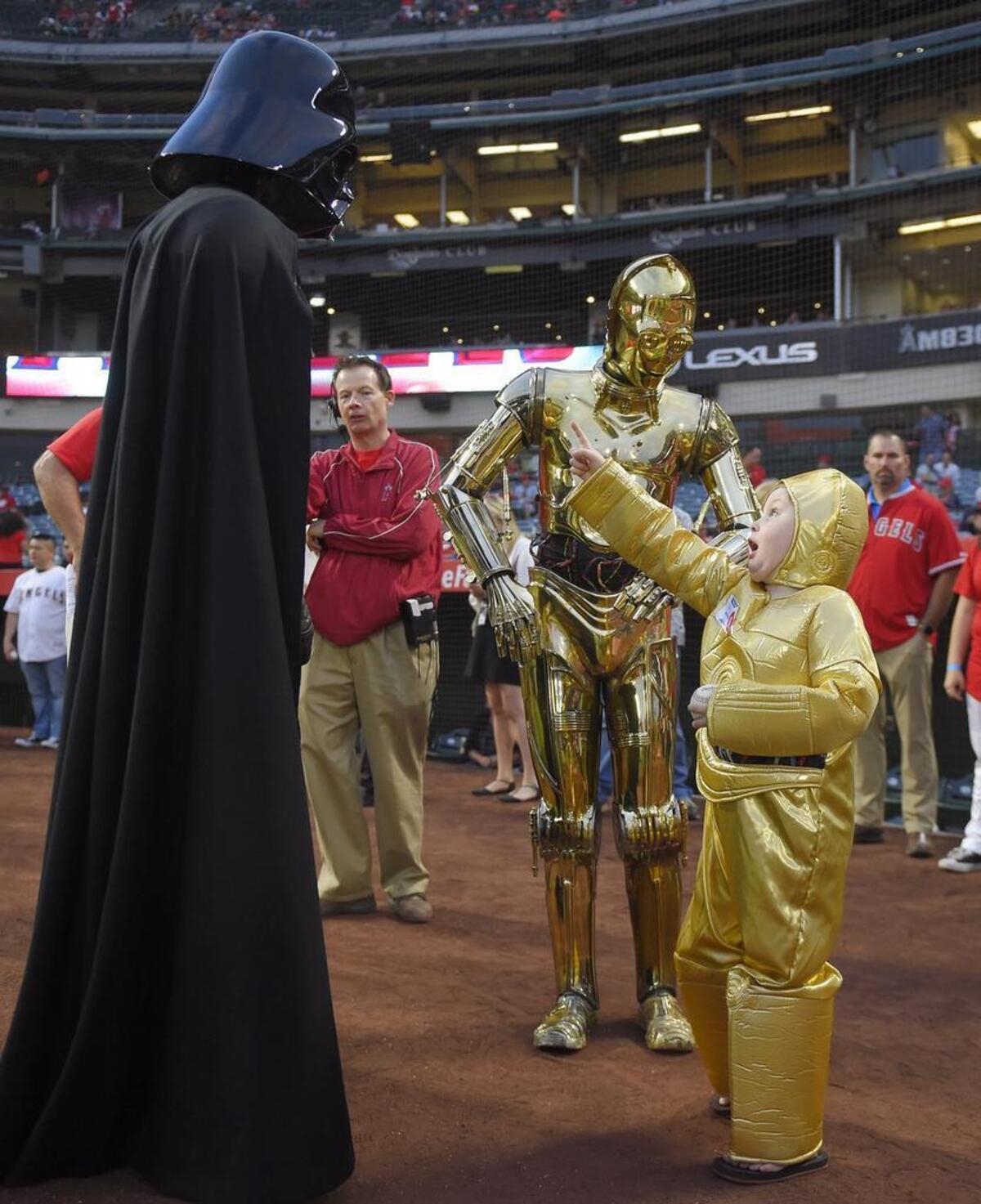Five-year-old Elijah Crandall, right, meets actors dressed up as Star Wars characters, Darth Vader, left, and C-3PO before the Rangers’ game against the Angels Friday night in Anaheim.