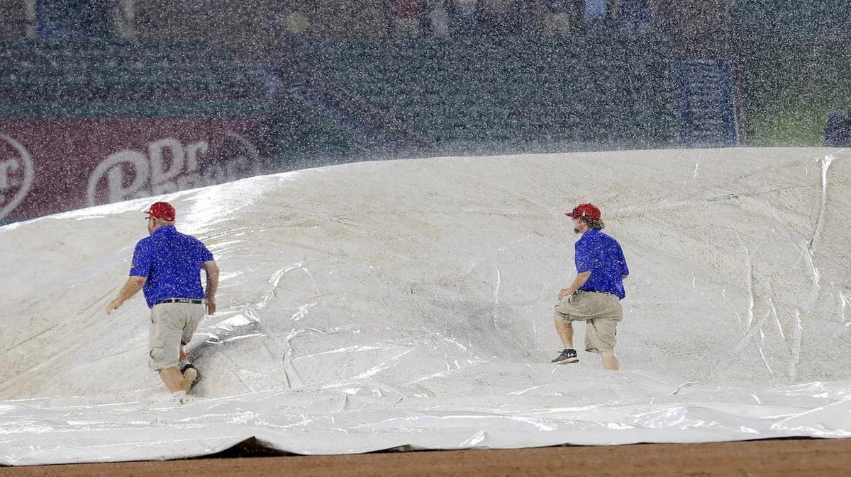 Grounds crew personnel walk over the field tarp to remove the air caught beneath as they place it over the field at Globe Life Park Wednesday night. The game was delayed by rain for about 40 minutes and resumed at 9:42 p.m. with the Rangers leading the Mariners 5-1 in the seventh.