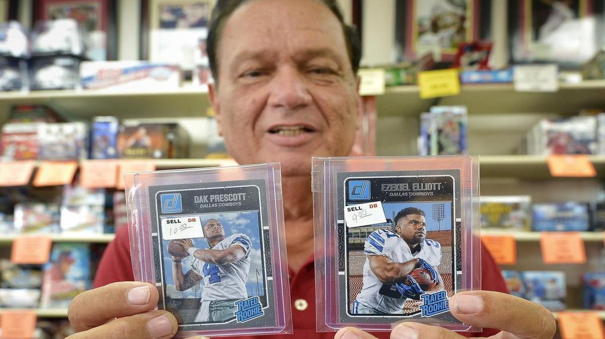 Duane Bates holds Dallas Cowboys quarterback Dak Prescott (4) and running back Ezekiel Elliott (21) rookie cards at Duane's Sports Cards in Arlington.