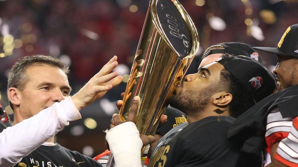 Ohio State Buckeyes running back Ezekiel Elliott kisses the trophy with coach Urban Meyer at left after a 42-20 victory over Oregon in the CFP National Championship in Arlington,Texas, Monday, Jan. 12, 2015.