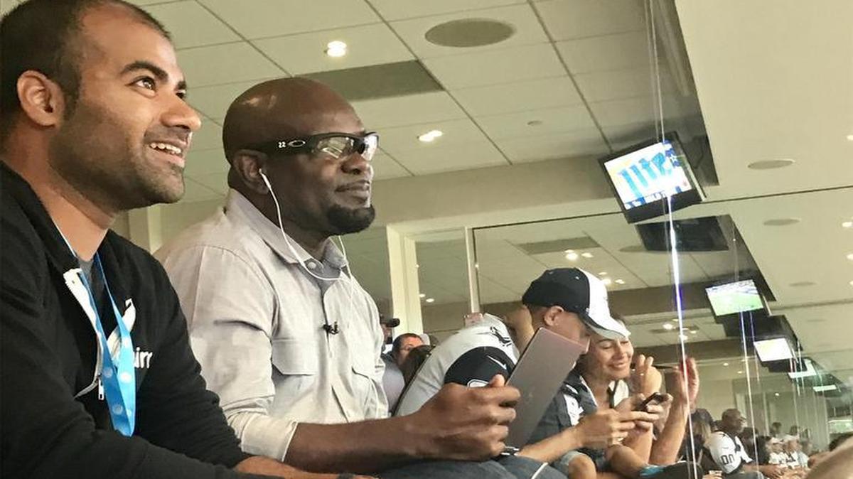 Emmitt Smith uses Aira to give play-by-play of the Cowboys-Rams game to a blind fan (not pictured) as Aira CEO Suman Kanuganti, left, watches.