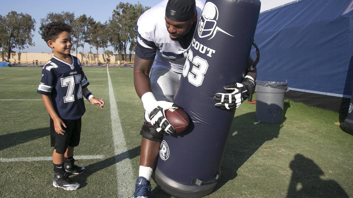 Cowboys offensive tackle Tyron Smith shows his 5-year-old son, Jaxson, how to hit a tackling dummy after practice Tuesday.