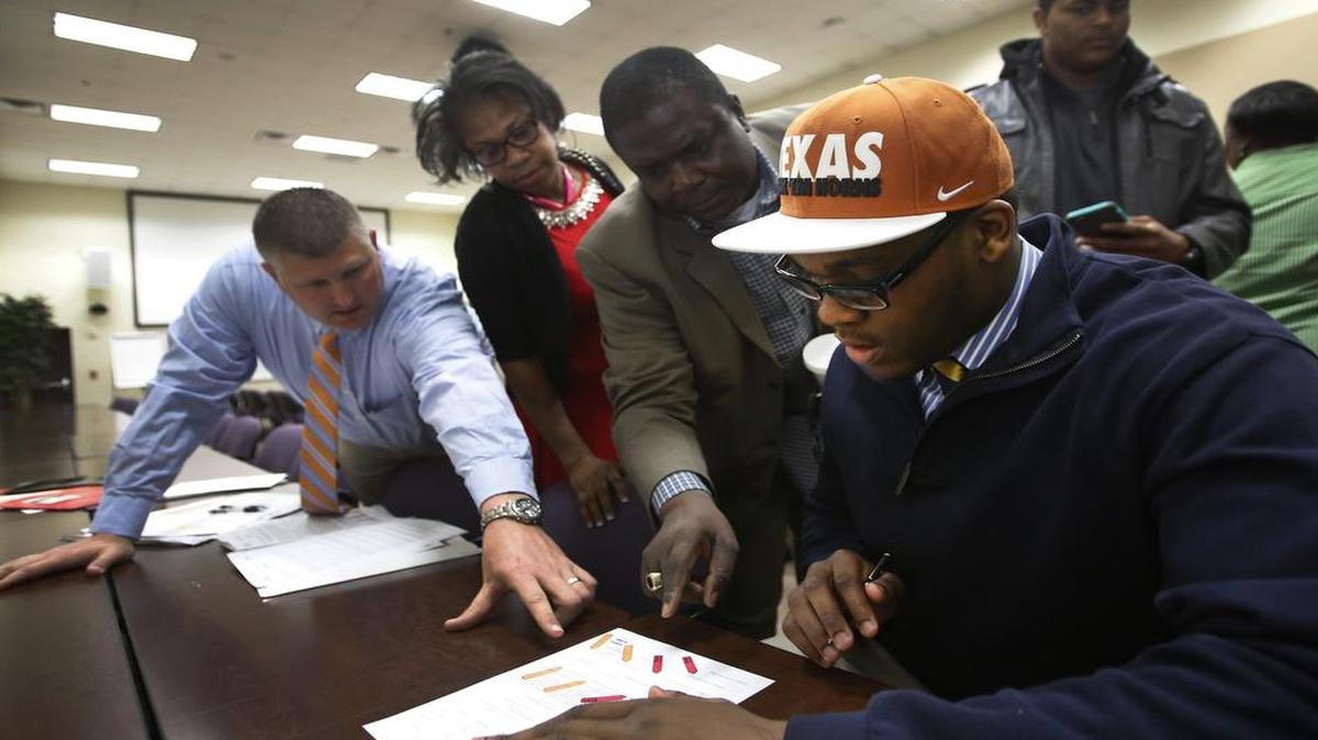 Arlington Bowie football player Tope Imade gets help from a Bowie coach, Nate Van Cleave, left, and mom and dad, Betty and Felix Imade, during National Signing Day last year.