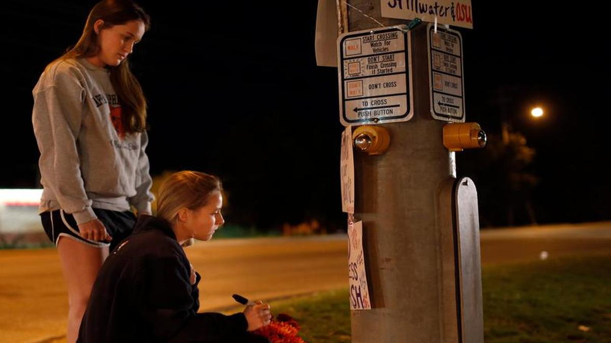 Oklahoma State students Kelly Cooke, right, and Rebecca Buchanan read messages on a memorial in Stillwater, Okla., Saturday, Oct. 24, 2015, near where a car crashed into spectators during the Oklahoma State University homecoming parade killing multiple and injuring several others.